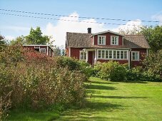 Garten mit rotgestrichenem Holzhaus und weissen Fenster