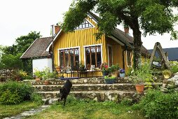 A wooden, yellow detached house with a terrace and a garden