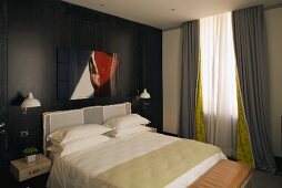 Schlafraum mit Doppelbett vor schwarzvertäfelter Holzwand und bodenlangen grauen Vorhängen am Fenster