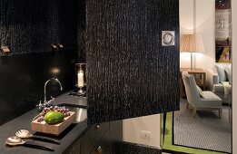 Offenstehende Tür einer schwarzen Schrankküche mit Spüle in Küchenzeile und Blick in Wohnraum