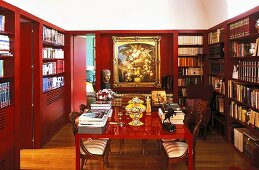 Red lacquered table in a library with red paneled walls and built in book shelves
