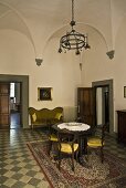 Vaulted ceiling in the salon of a villa with antique furniture on a floor with checkerboard pattern and a view of an open door