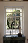 Palmenblätter in Vase und Steinfigur vor Sprossenfenster mit Blick in Garten