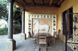 Loggia of a country home with black columns and antique wooden patio furniture in front of a horse in white relief