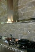 Stainless steel kitchen countertop with integrated stove and extractor fan in front of a natural stone wall