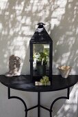 Lantern and ceramics on a black console table in front of a white house facade