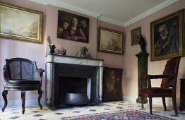 Living room in an old building with antique chairs in front of a fireplace with paintings on a pink wall