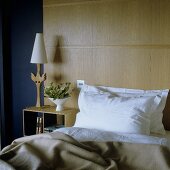 Bett vor holzvertäfelter Wand und Nachttisch mit Tischlampe