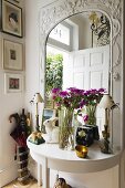 A bunch of flowers on a white wall table in front of a mirror with a carved wooden frame
