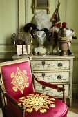 Barocker Holzstuhl mit goldenem Muster auf rotem glänzenden Bezug vor bemalter Kommode