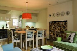 An open-plan living room with a ceiling lamp with an orange shade above a dining table and a fireplace stacked with wood