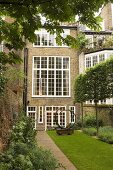 An English residential house with white transom windows and a sculpture in a turfed courtyard