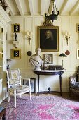 An antique chair and a wall table against a white, wood panelled wall in the corner of a living room