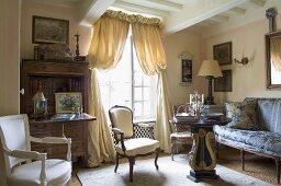 A classic country style living room with antique seats and a window with a gathered curtain