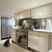 A designer, open-plan fitted kitchen with a lowered ceiling - spotlight illuminate the white cupboards with stainless steel handles