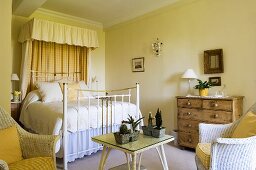 A country house-style bedroom with yellow walls and a white brass bedstead with a canopy