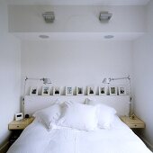 Bett mit weisser Bettwäsche und Bildergalerie in Wandnische und schwenkbaren Tischleuchten