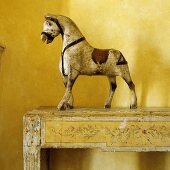 A painted wooden horse on a wooden console in front of a yellow wall