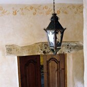 Ceiling lantern in front of an apricot colored wall with border and wooden lentil over a door to a room