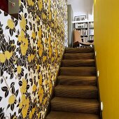 Schmaler Treppenaufgang mit Blumenmuster auf Tapete und gelber Wand mit Blick auf Stuhl