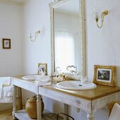 A simple washstand with two basins and a white framed, illuminated mirror in the bathroom of a country house