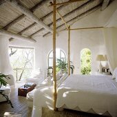 Rustikale Holzdecke mit weißem Himmelbett aus Bambuskonstruktion und Ausblick in den Garten