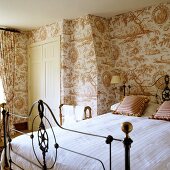 Bedroom with antique iron bed in front of wall covered with patterned wallpaper (country home style decor)