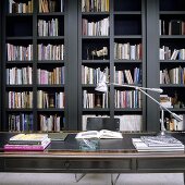 An antique desk with a leather writing pad in front of a grey wooden bookshelf