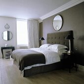 A double bed with a high, upholstered headboard against a dark wall with a mirror hanging above it