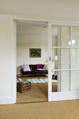 A hallway with an open sliding door and a view of a leather sofa in a living room with a sisal floor