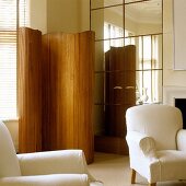 A curved paravent and a white armchair in front of a cupboard with a mirrored front