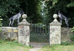 Two dogs standing on a weathered stone wall with a garden gate
