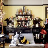 A large collection of vases on a black sideboard against a yellow wall