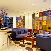 A purple sofa in front of a mirrored wall and a large abstract picture of bright coloured circles