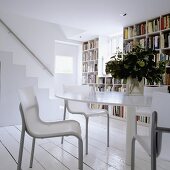 A round table with chairs in front of a bookshelf wall with a stairway in the background