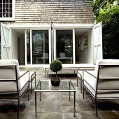 Metal terrace furniture with white cushions facing a bank of windows with open shutters