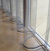 A transparent, grey curtain at the window and a wooden floor