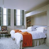 Orange throws on two single beds in a room with windows with shutters on the inside