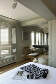 Shirt on a bed and chair in front of a bright gray, paneled bedroom wall