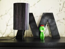 Table lamp with black shade and green toy on a black surface