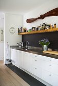 Kitchen unit with stainless steel work area and base cabinets with white fronts in front of a black back splash