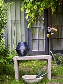 A blue lantern on a stone bench and bowl of garden tools in front of a garden shed