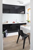 Blick in Küche mit schwarzen Hochglanzfronten, weißem schmalem Esstisch & schwarzem Kunststoffstuhl