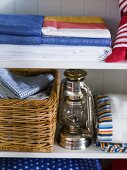 Bed linen and basket with laundry next to a kerosene lamp in white cupboard