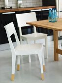 White kitchen chairs in a dining area in front of a kitchen unit with black base cabinets