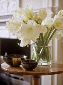 A detail of a traditional sitting room, showing a round wooden side table, lily flower arrangement, bowls