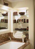 A detail of a traditional bathroom, showing a fitted bath with marble surround, glass shelves in recess