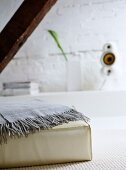 Throw draped on cushion in white sitting room with exposed wooden beam and ledge.