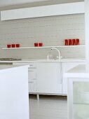 Modern white kitchen with red glassware on shelf above cupboard units.