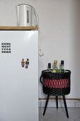 Wasserkocher auf Kühlschrank und Korb mit Flaschen auf Hocker